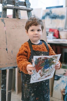 A young child displaying colorful artwork in an art classroom.