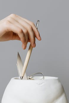 Close-up of a hand with sculpting tools in a ceramic vase, showcasing craft making.