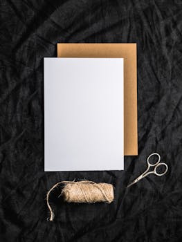 Flat lay of blank sheets, scissors, and twine on black fabric, perfect for mockups.