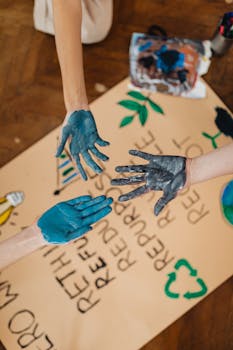 Hands covered in blue paint creating art with environmental themes on paper.