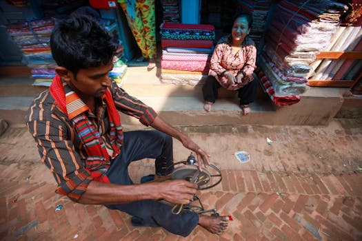 Man operates foot-pedaled sewing machine beside a vibrant fabric shop in an outdoor market.