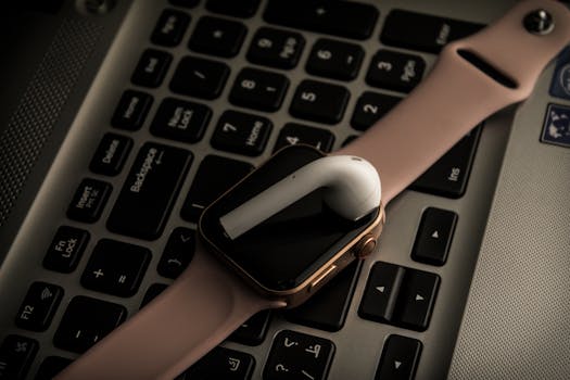 Close-up of a smartwatch and earpod on a laptop keyboard - modern technology essentials.