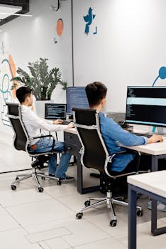 Two programmers collaborating in a bright, modern office, coding on monitors.